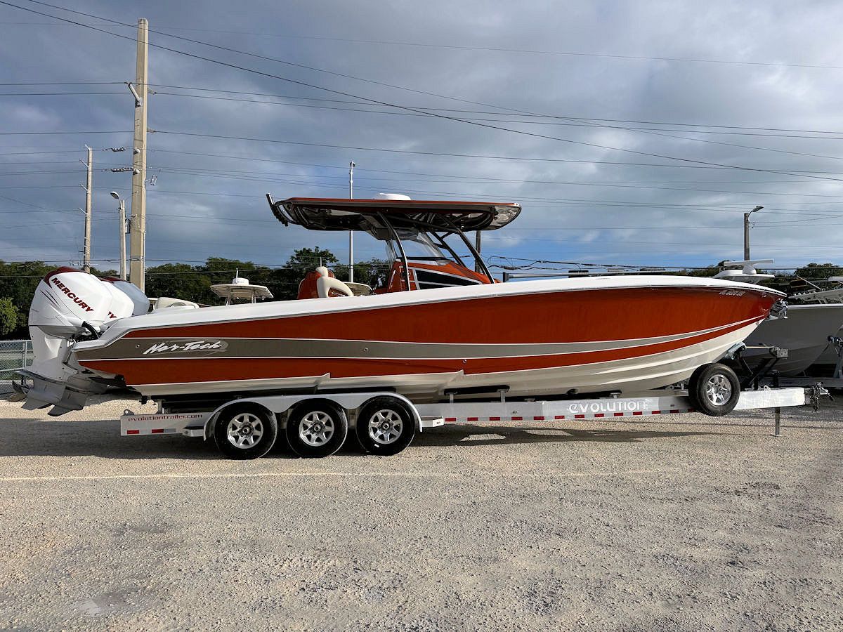 Orange and white powerboat on a trailer, parked on a paved lot.