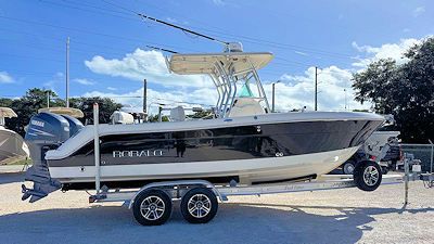 Boat on a trailer, parked on pavement, under a blue sky. It has two outboard motors.