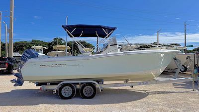 A white boat on a trailer, blue canopy, parked on gravel. Sunny day, with blue sky.