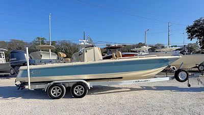 Blue and tan boat on a trailer, parked on a gravel surface under a blue sky.