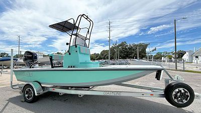 A light green and gray boat on a trailer, under a partly cloudy sky.