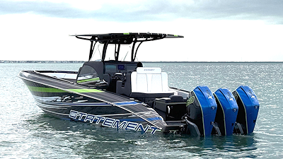 Black and green speedboat with three blue outboard motors floating in the ocean.
