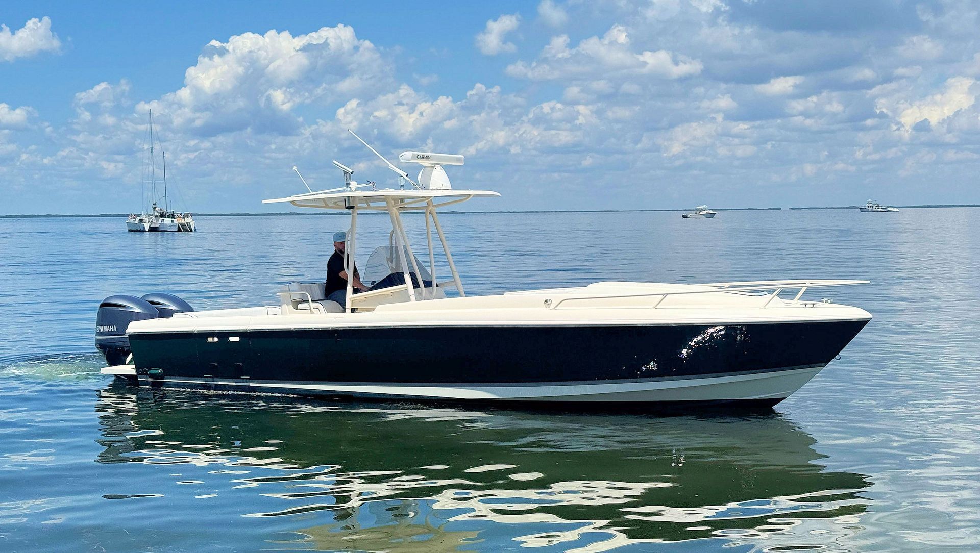 White and navy center console boat floating on calm blue water under a partly cloudy sky