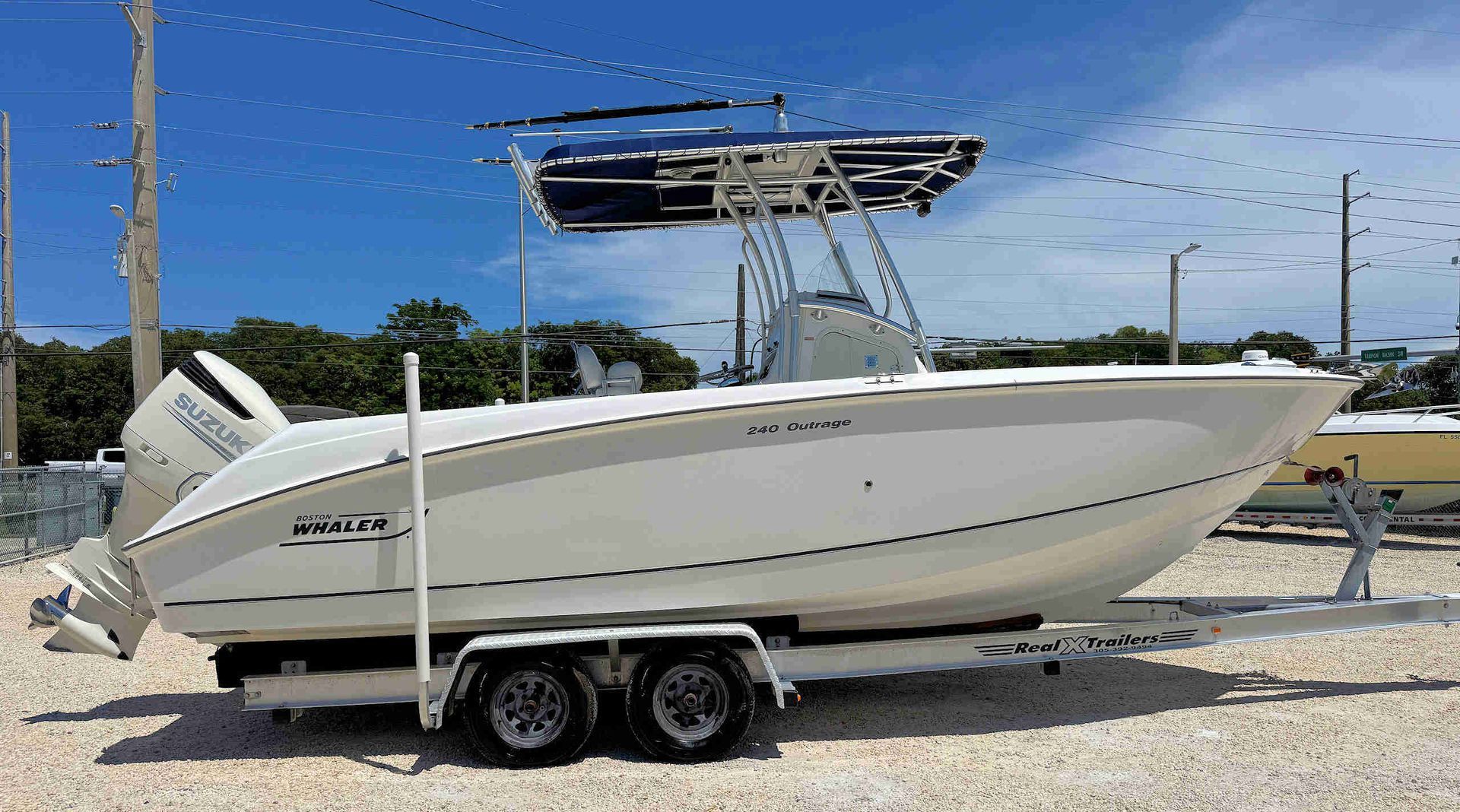 White center-console fishing boat on a trailer parked outdoors under a blue sky.