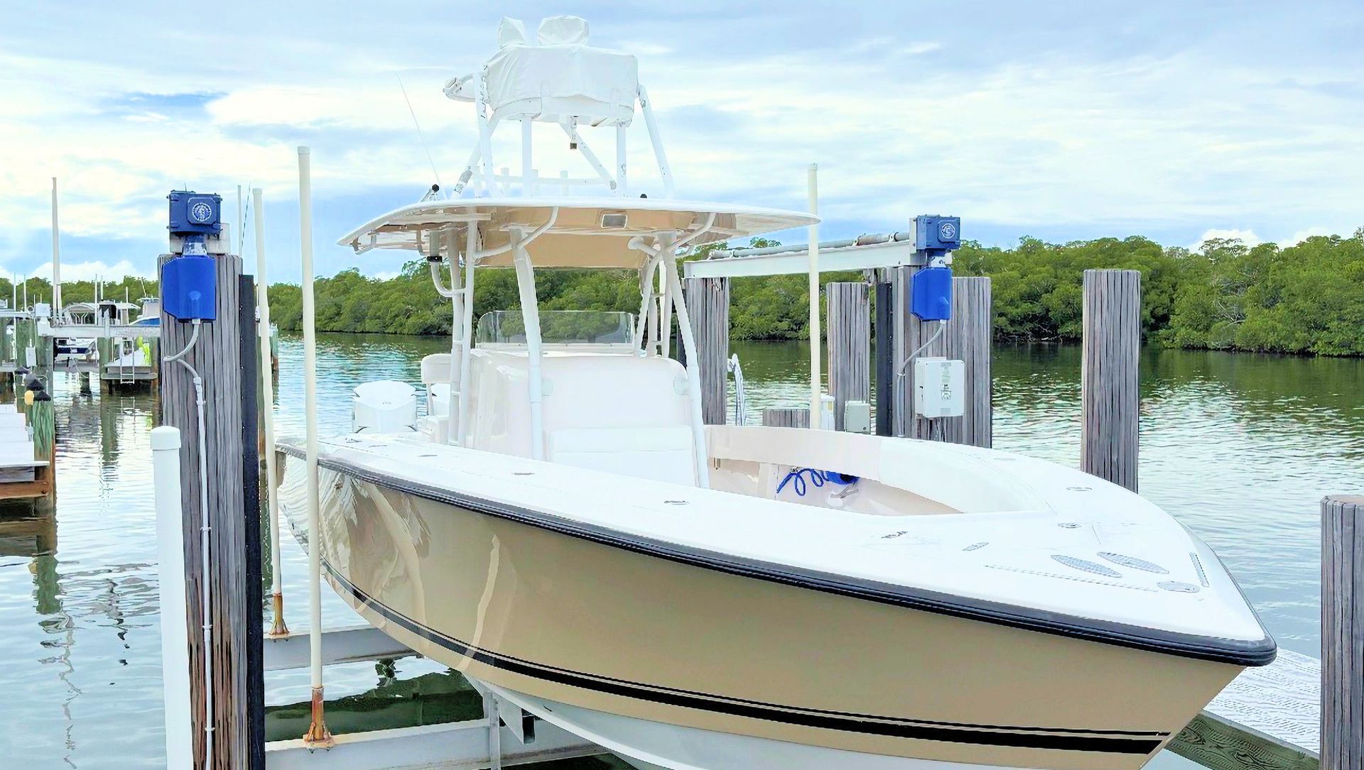 White center console boat in a boat lift beside calm water, with a T-top and blue accents
