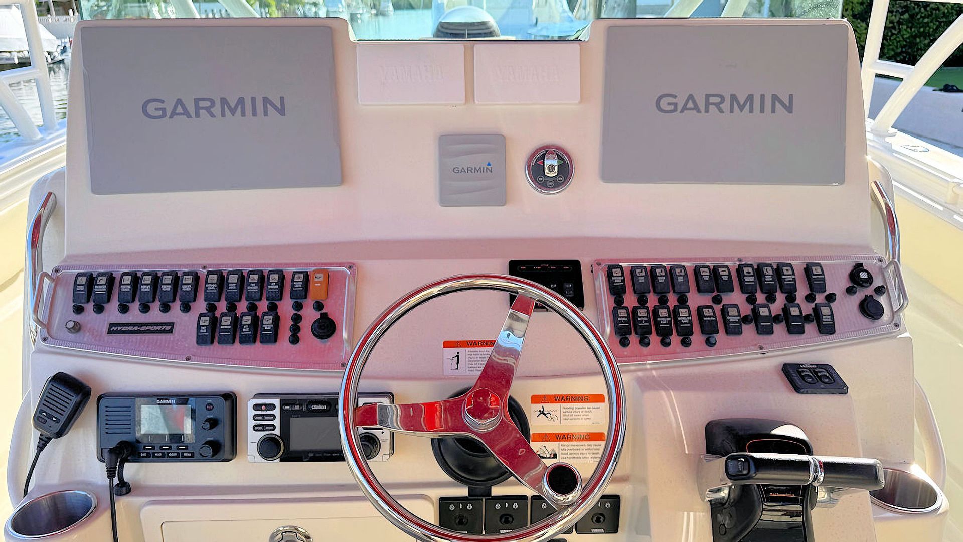 Boat helm with twin Garmin displays, steering wheel, and rows of switches and controls