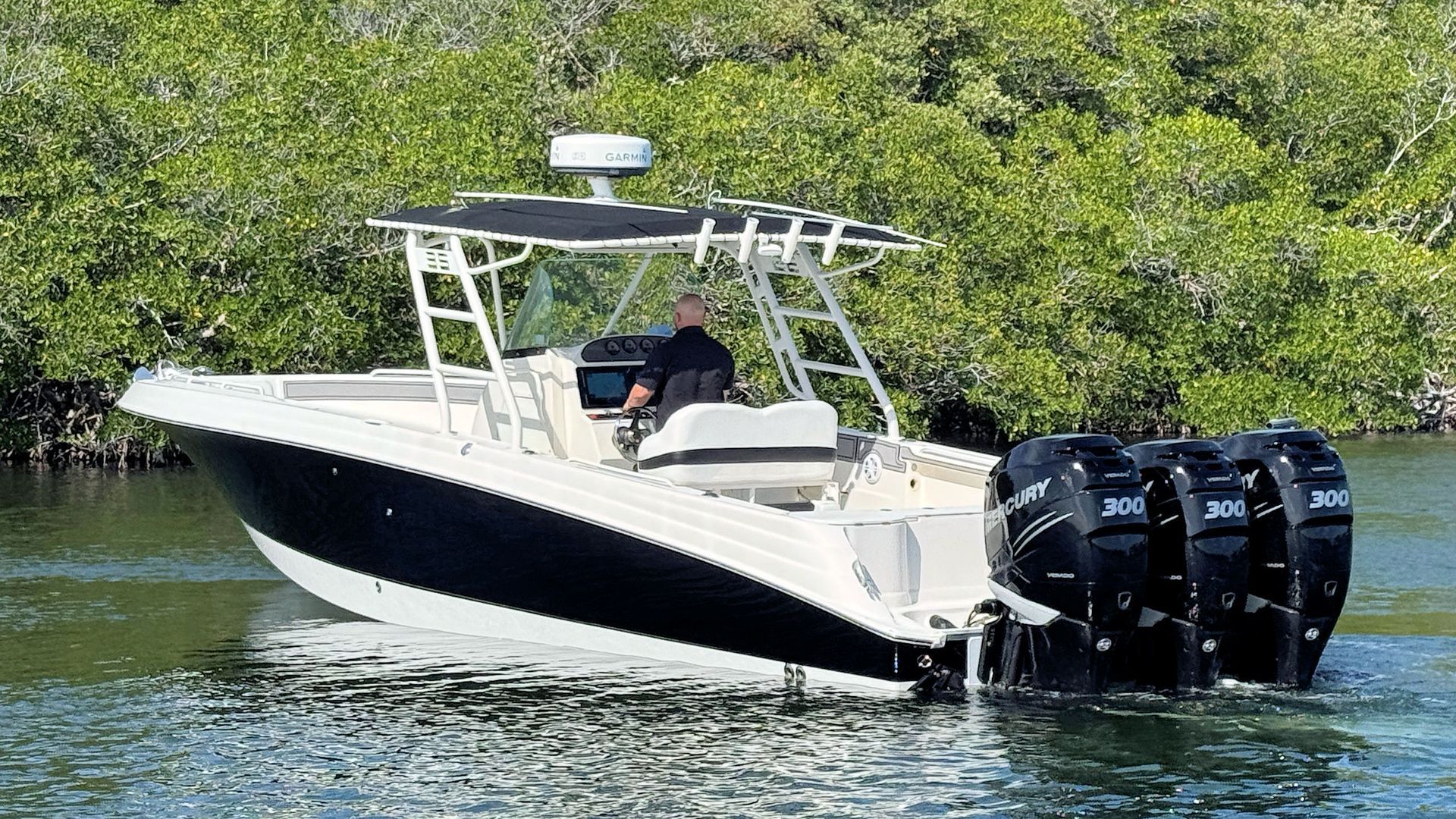 White Wellcraft center console boat cruising on calm water with twin outboard engines and green shoreline behind