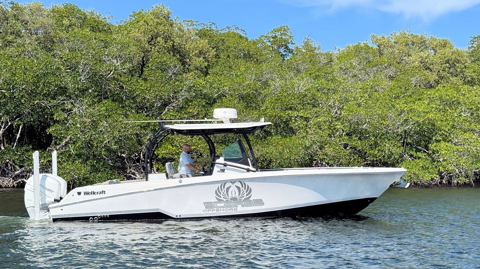White center-console boat on calm water near mangrove shoreline under a bright blue sky