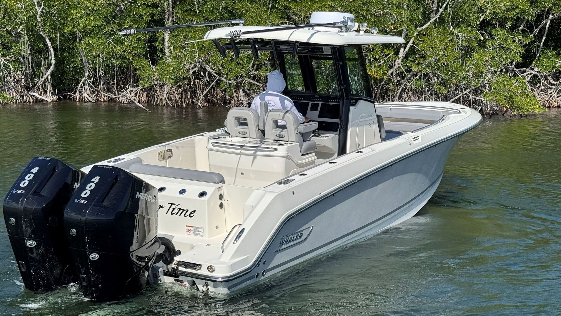 A white Boston Whaler center console boat with dual outboard engines cruising through water near mangroves.