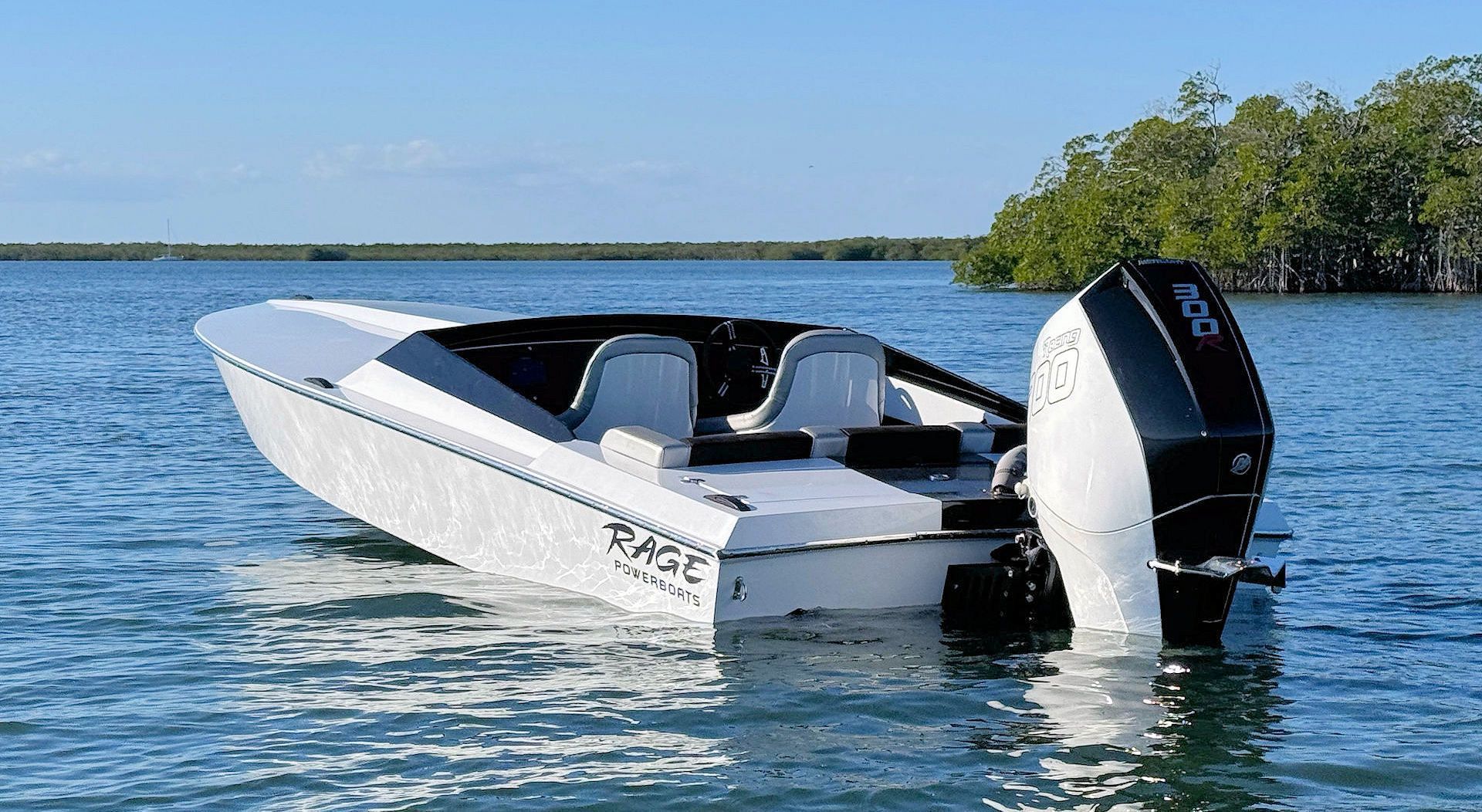 A sleek white motorboat with a black outboard engine floating in calm water near a treelined shore.