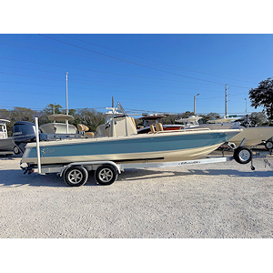 White speedboat on calm water with blue sky and light foliage in the background.
