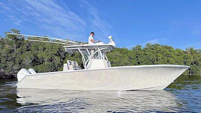 White fishing boat with a person at the helm, in a body of water with trees in the background.