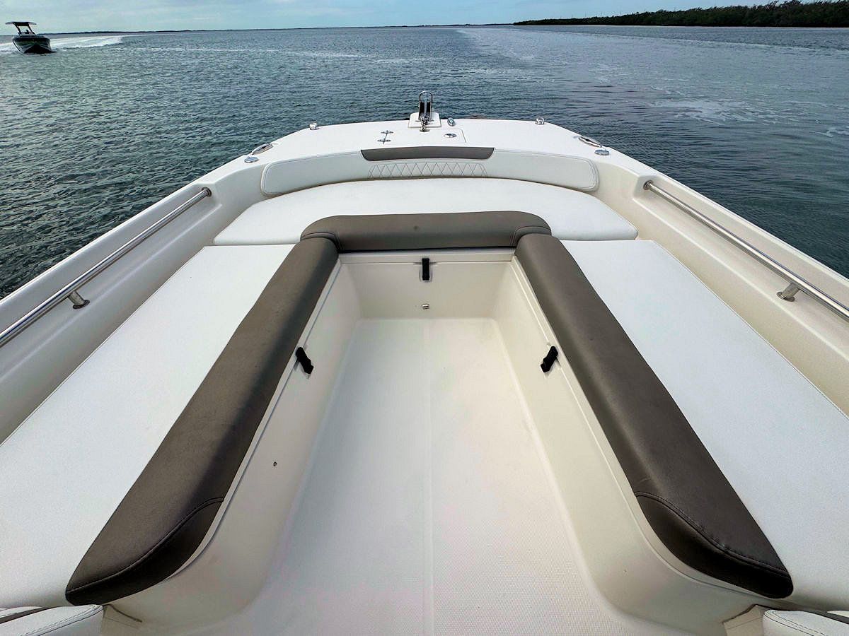 View from the bow of a boat with gray cushioned seating, facing out onto calm water.