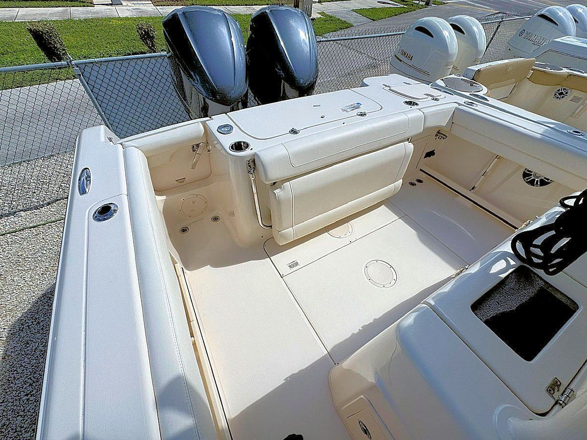 Boat deck with tan flooring, white seats, and blue outboard motors.