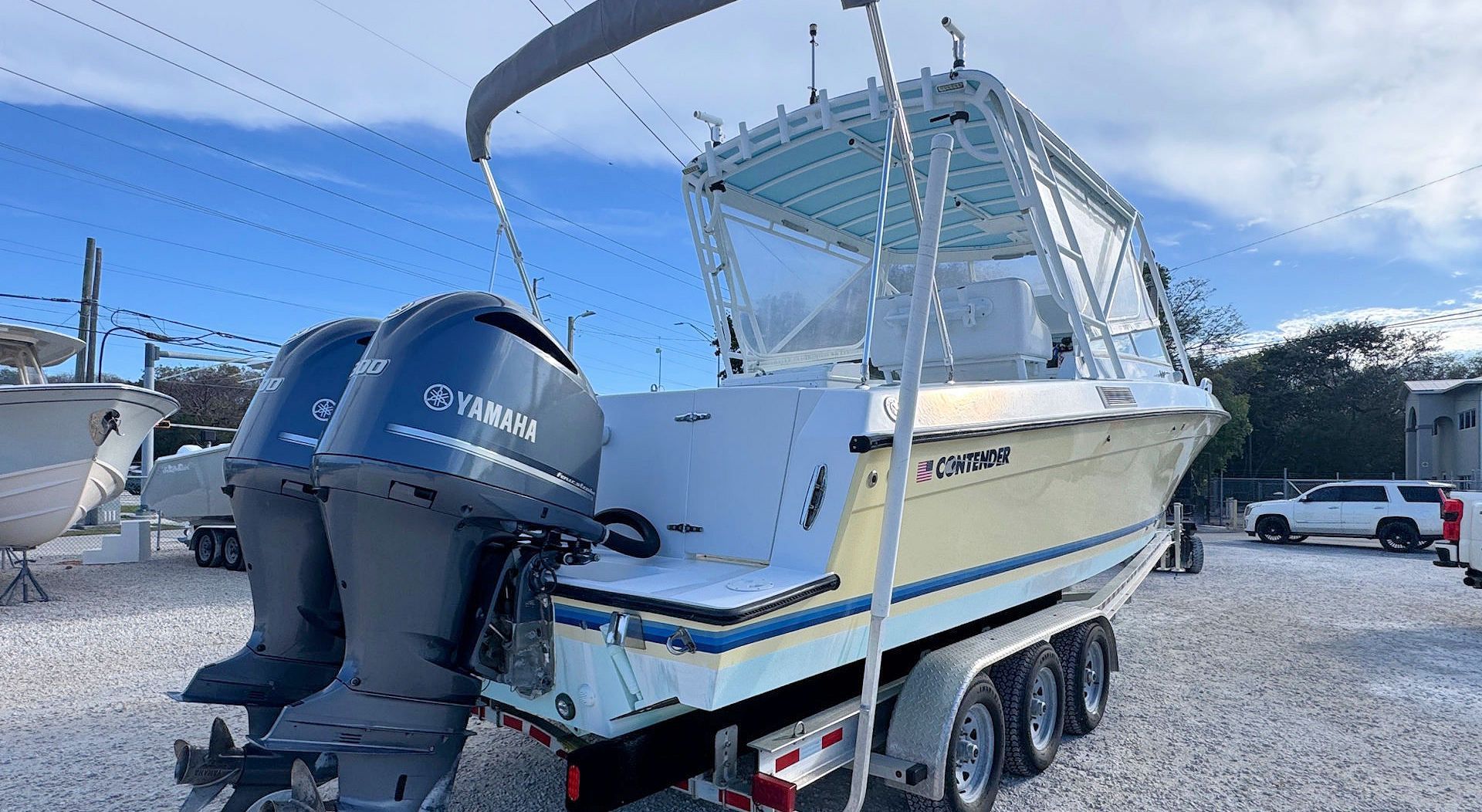 White fishing boat on trailer with Yamaha outboard, parked in gravel lot under clear sky