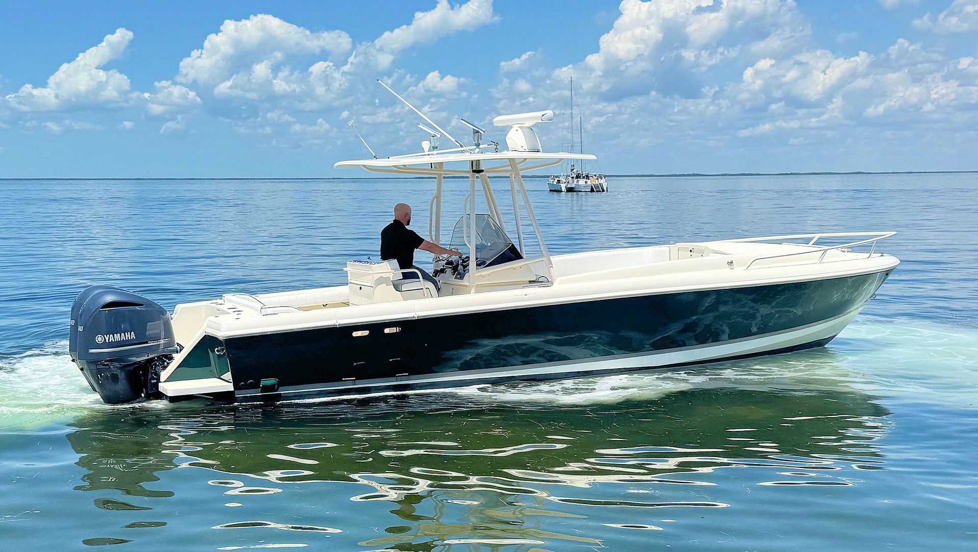 White and navy center console boat on calm blue water with one person aboard under a partly cloudy sky
