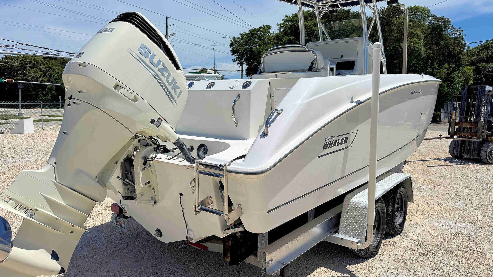 White center console boat on trailer in a gravel lot, viewed from the stern with outboard engine visible.