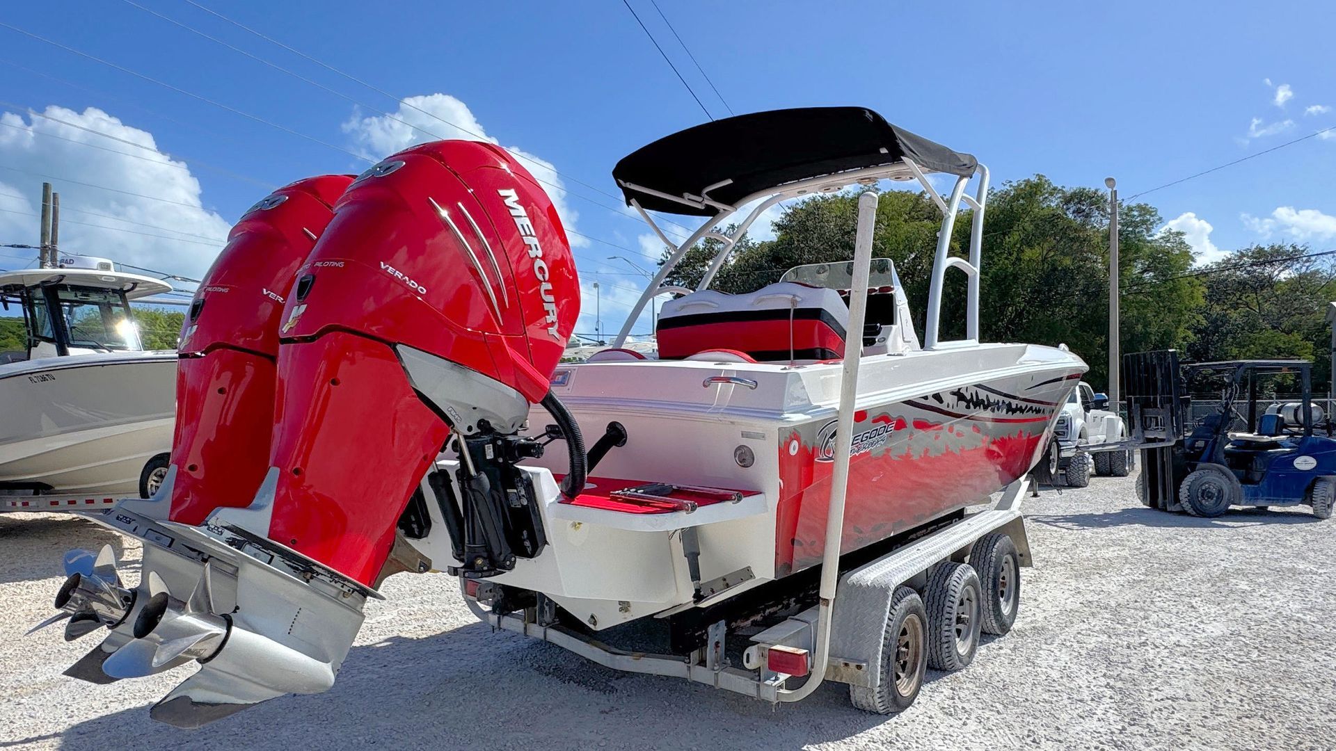 Red and white speedboat on a trailer at a marina, with a black bimini top under a blue sky.
