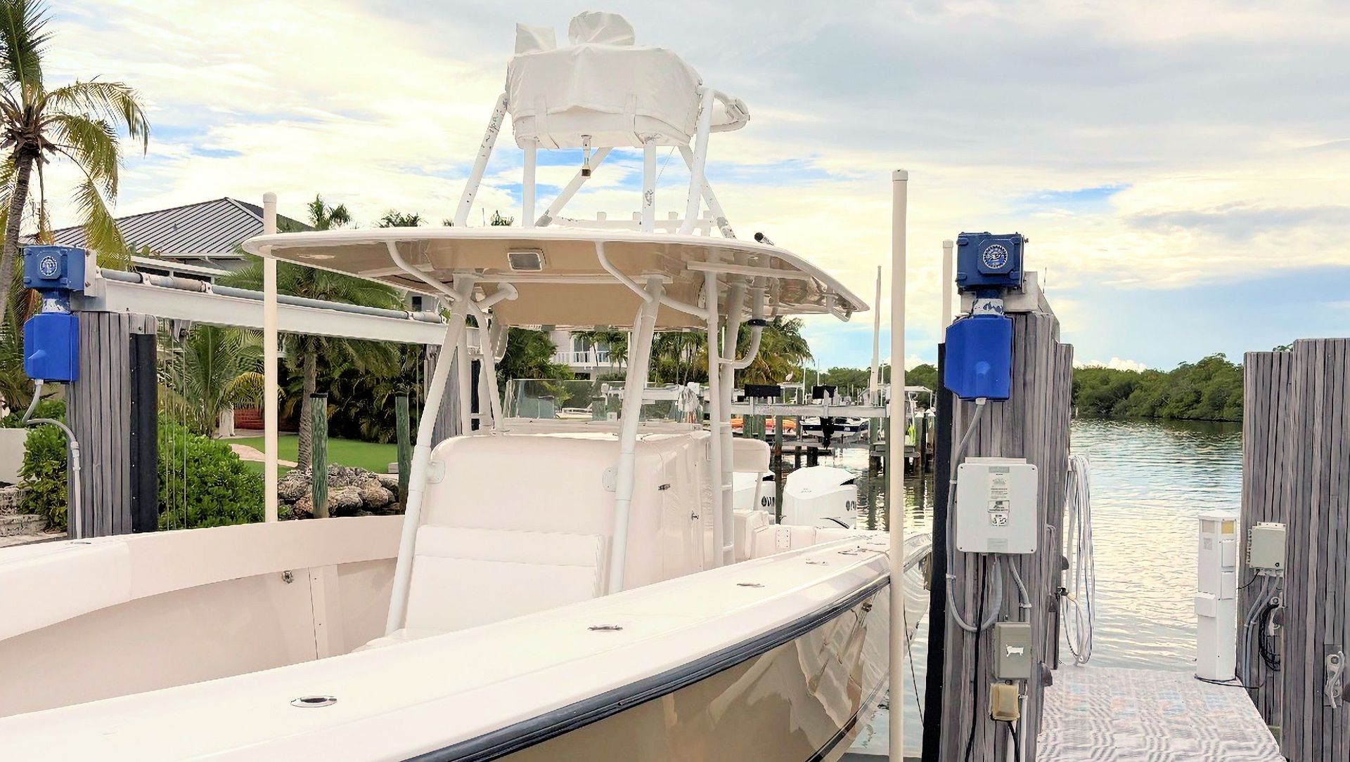 White fishing boat at a dock beside blue posts, with calm water and a marina in the background
