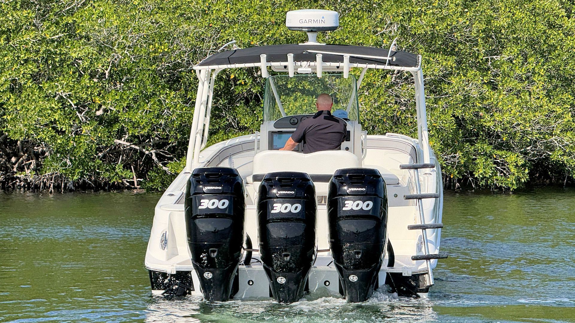 White center-console boat with three outboard motors cruising on calm water near mangrove shore