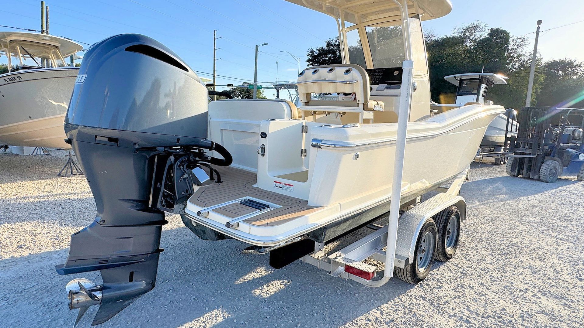 White center-console fishing boat on a trailer with a large black outboard motor in a sunny lot.