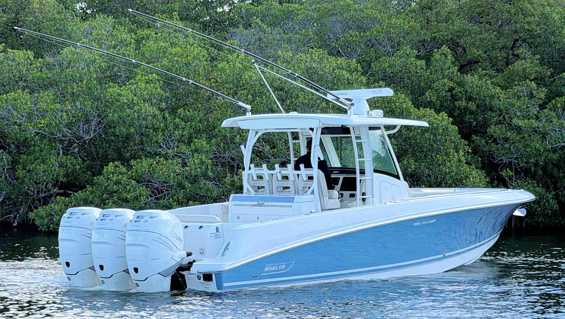 White center-console boat with three outboard motors on calm water near mangrove shore