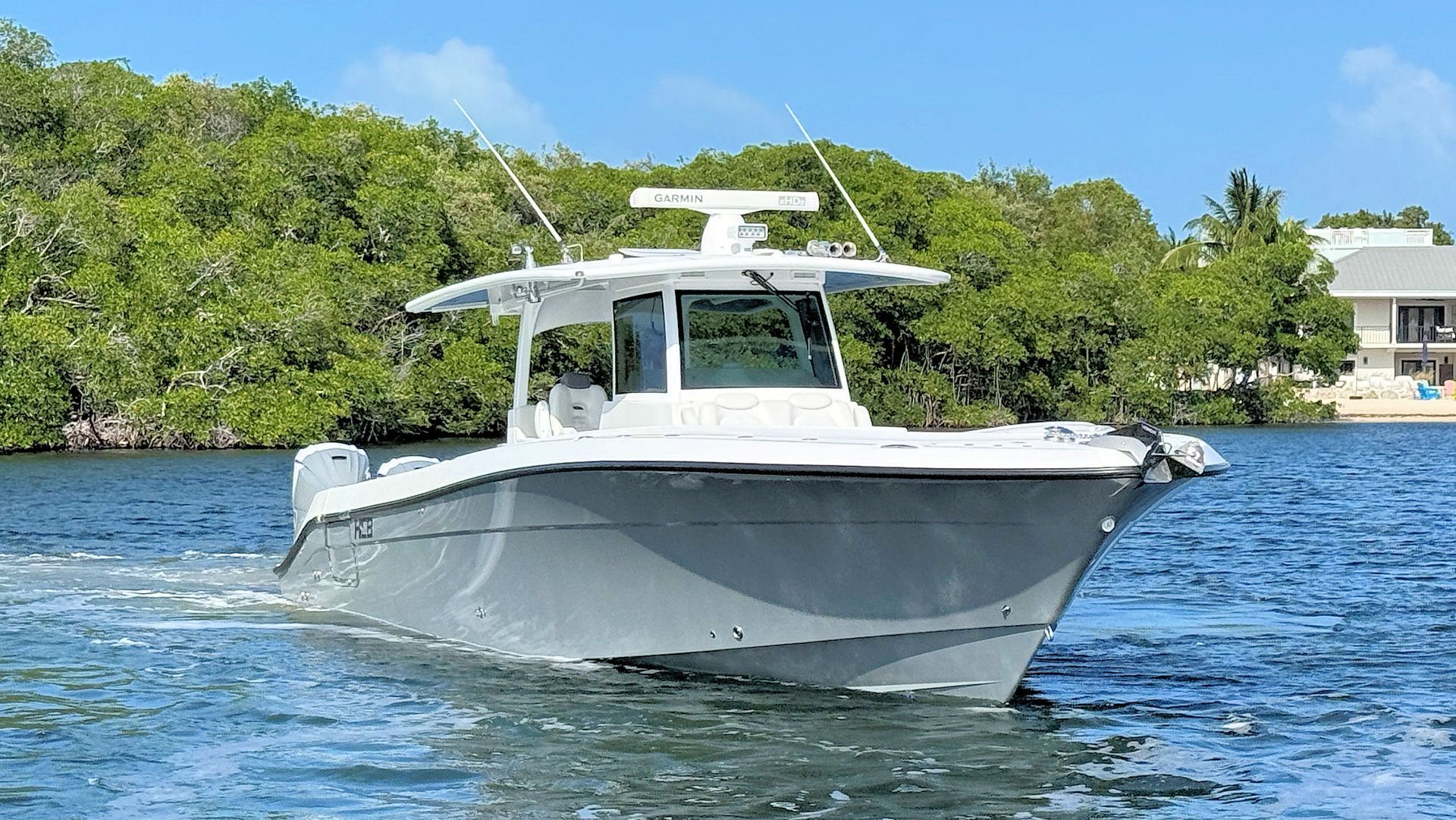 Center console fishing boat cruising on blue water near a lush green shoreline