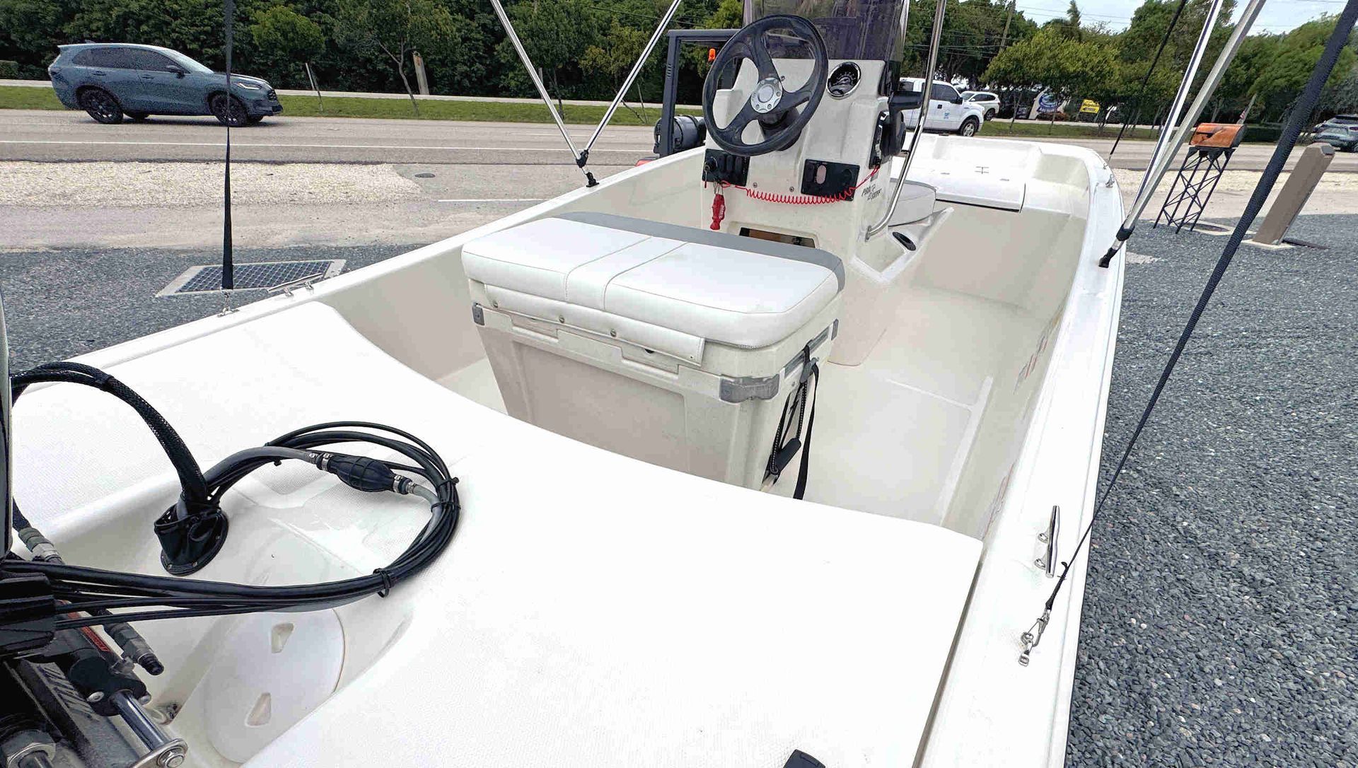 White fishing boat foredeck with center console, steering wheel, and gray seats on a gravel lot outdoors