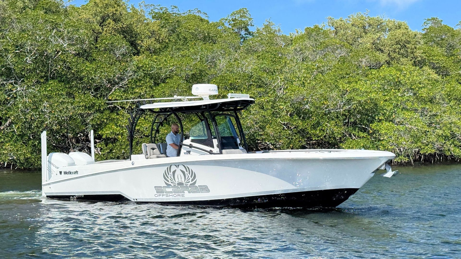 White fishing boat on calm water near mangrove trees, with two people aboard under a canopy.