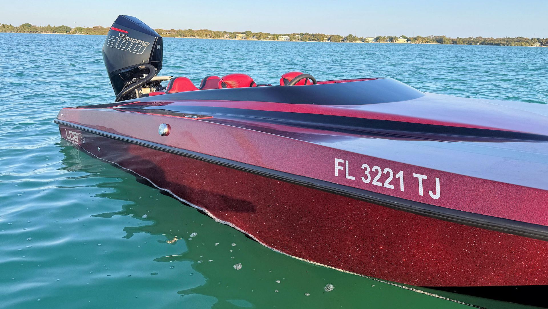 Red high-performance catamaran on calm blue water with Florida registration, viewed from the side.