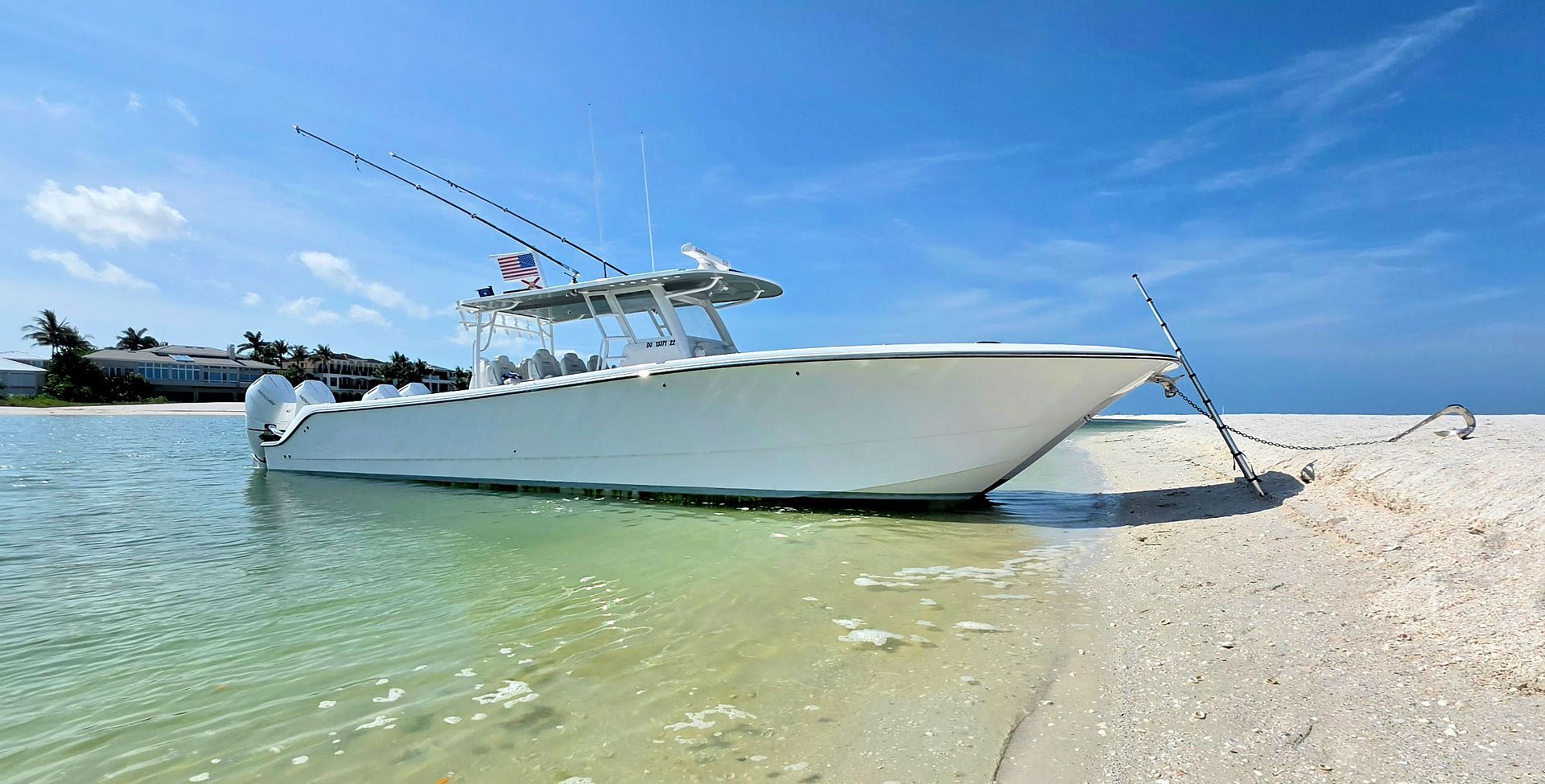 White center console fishing boat anchored in shallow turquoise water beside a sandy beach under a clear blue sky