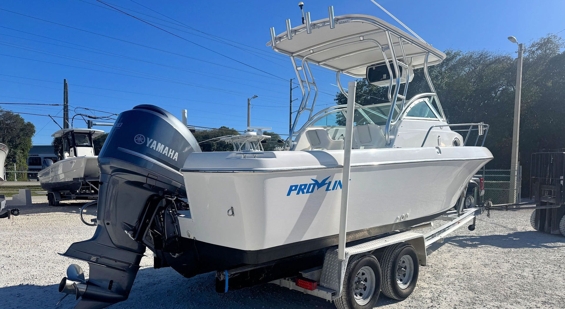 A white dual-console walkaround boat with a blue Yamaha outboard motor, mounted on a trailer in a sunny, outdoor storage lot.