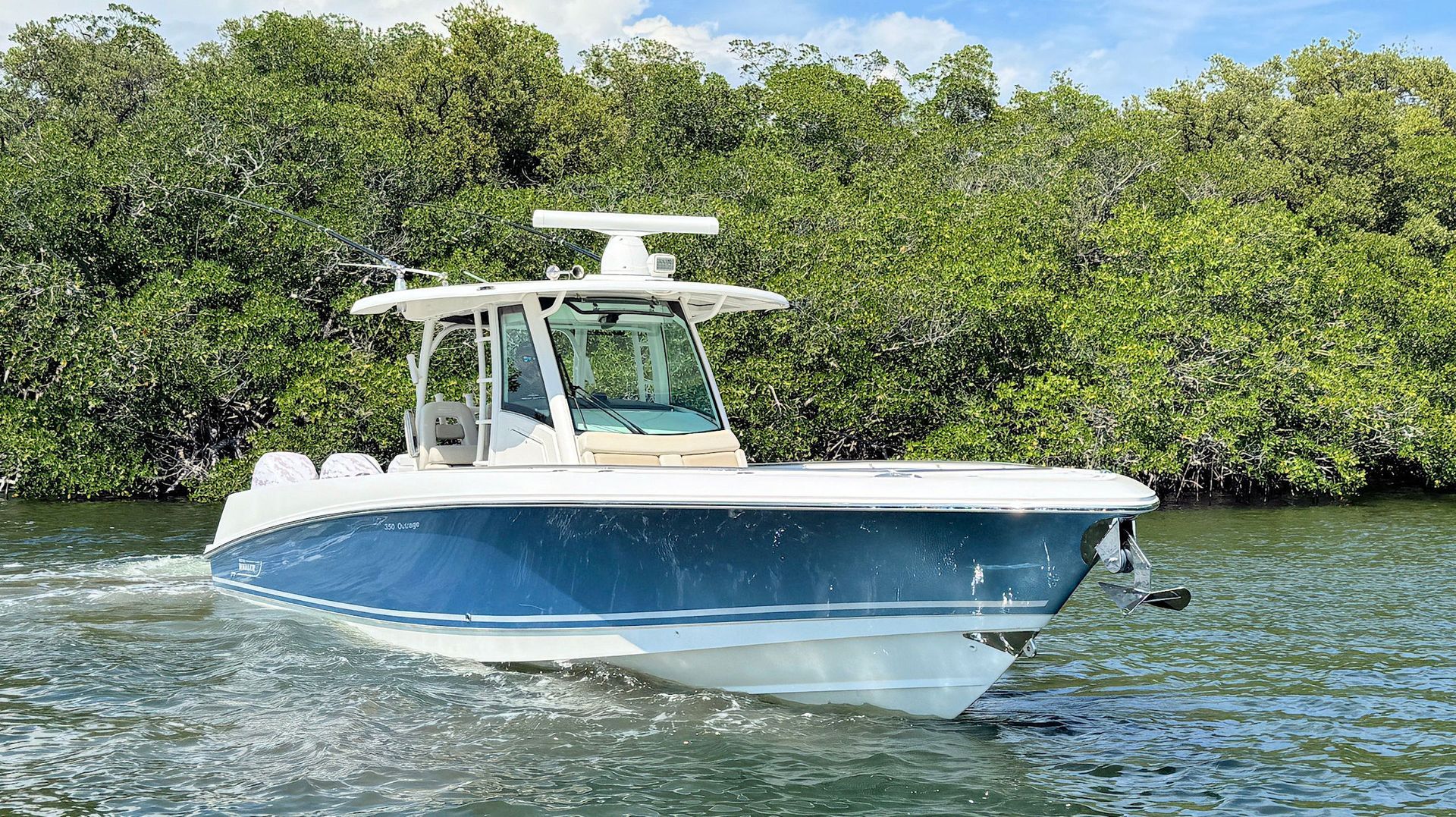 Blue and white center console  fishing boat cruising on calm water with mangrove shoreline in the background