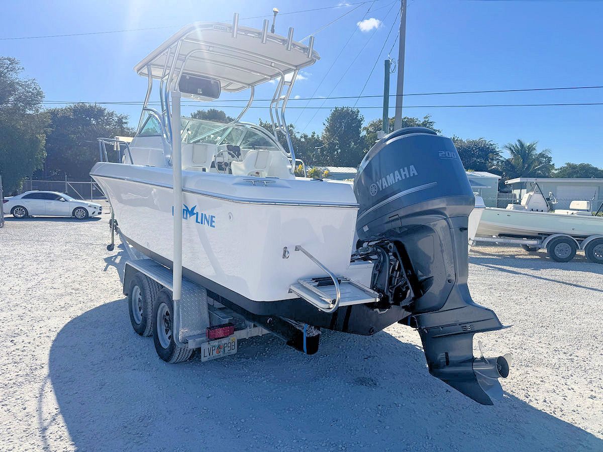 White boat on a trailer, blue Yamaha outboard motor, sunny day, asphalt, trees in background.