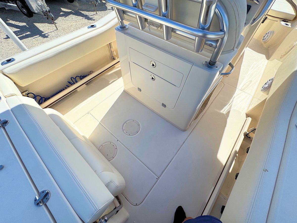 Boat interior with white seating, beige flooring, and a central console with metal railings.