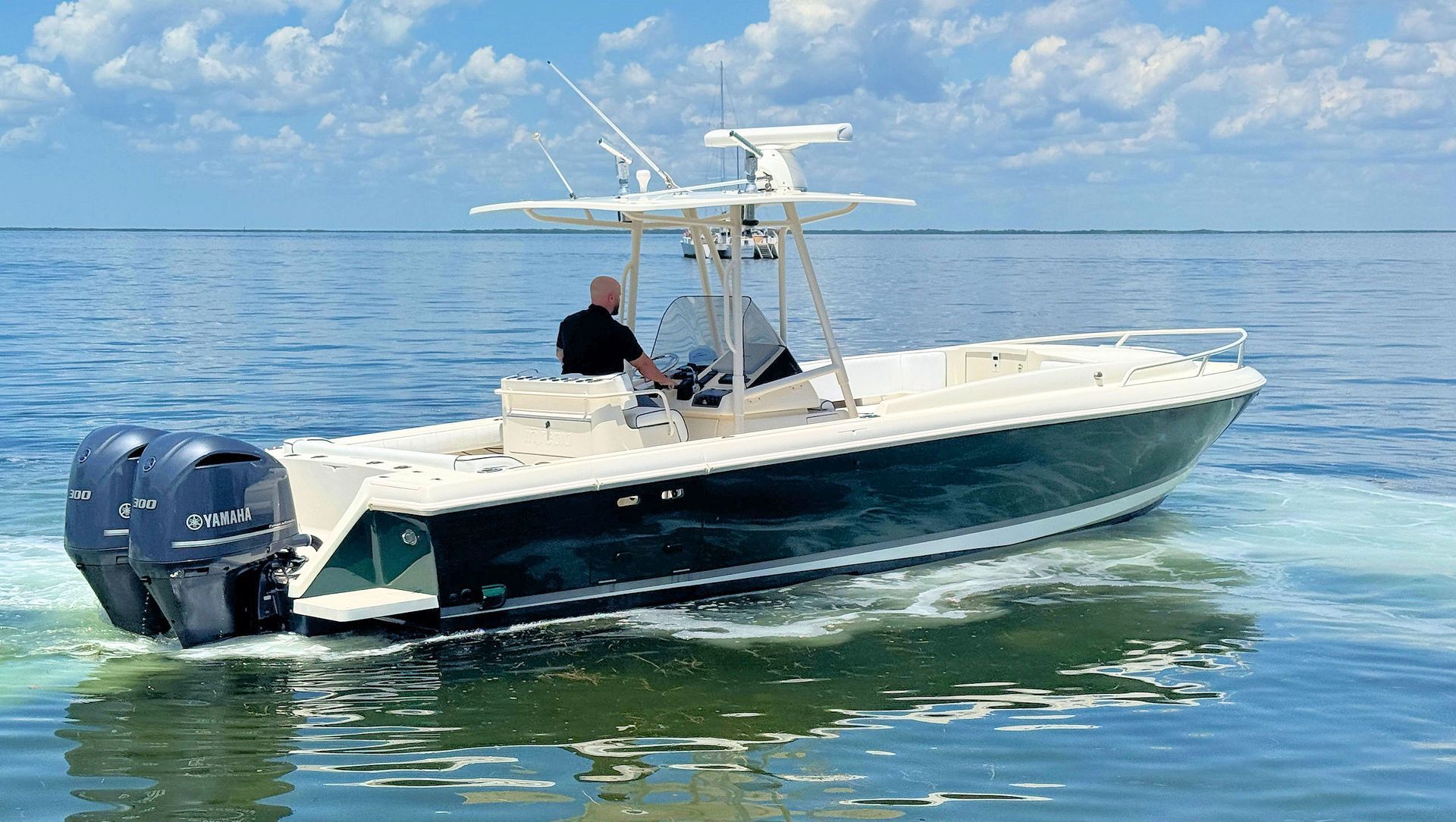 White and navy center console boat with a person aboard, floating on calm blue water under a bright sky.