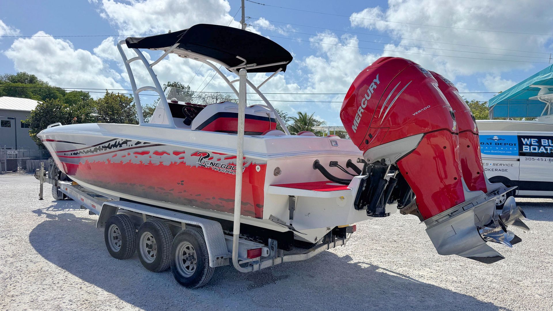 White and red motorboat on a trailer with a red outboard motor, parked on gravel under a canopy.