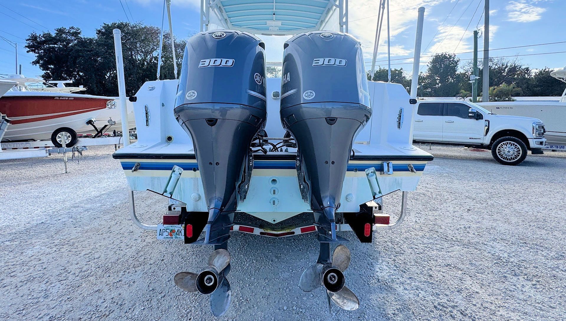 Two gray outboard motors on a white boat at a marina, with trailers and boats in the background