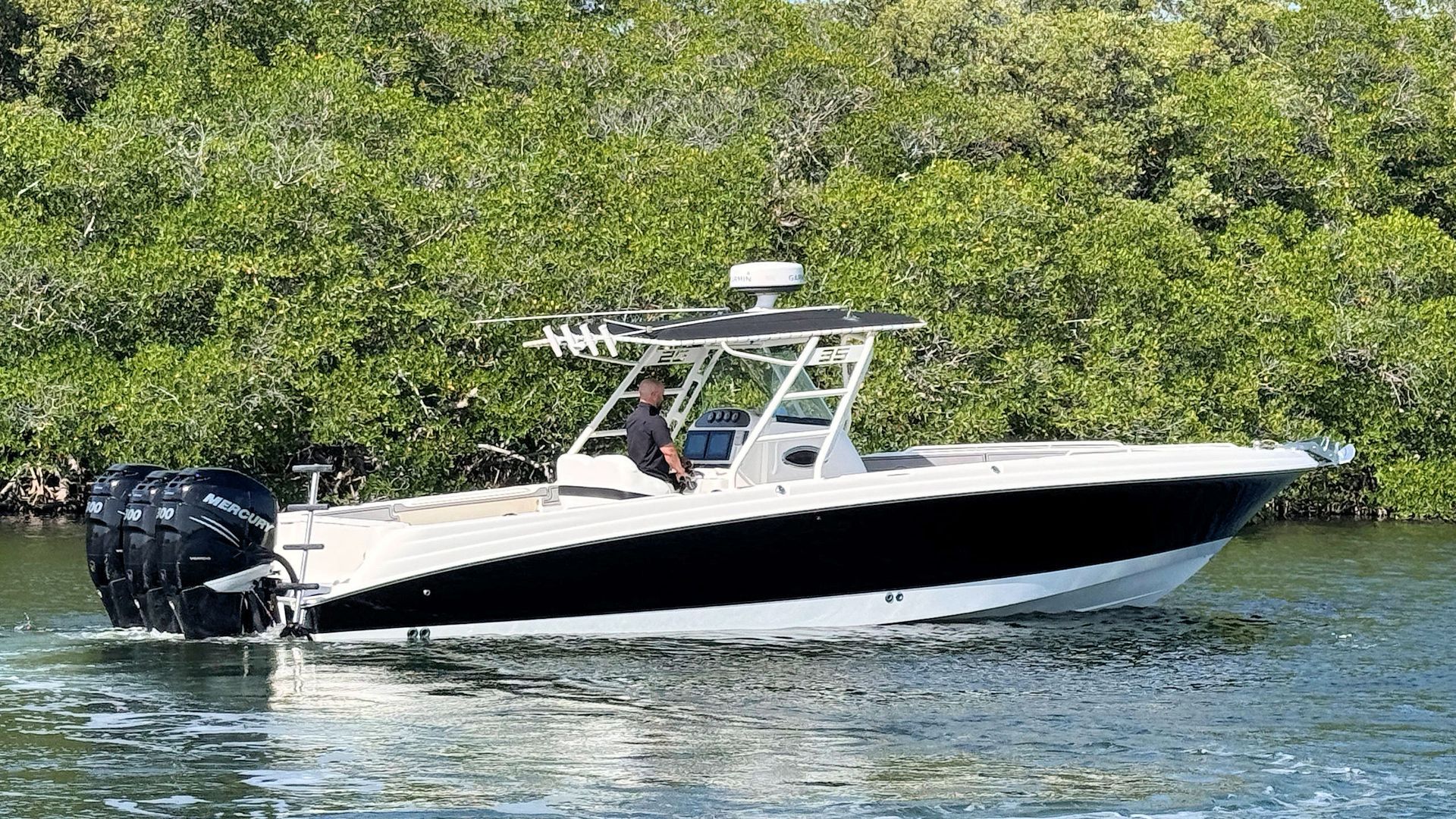 Wellcraft center console boat cruising on calm water near a green shoreline, with a black outboard motor.