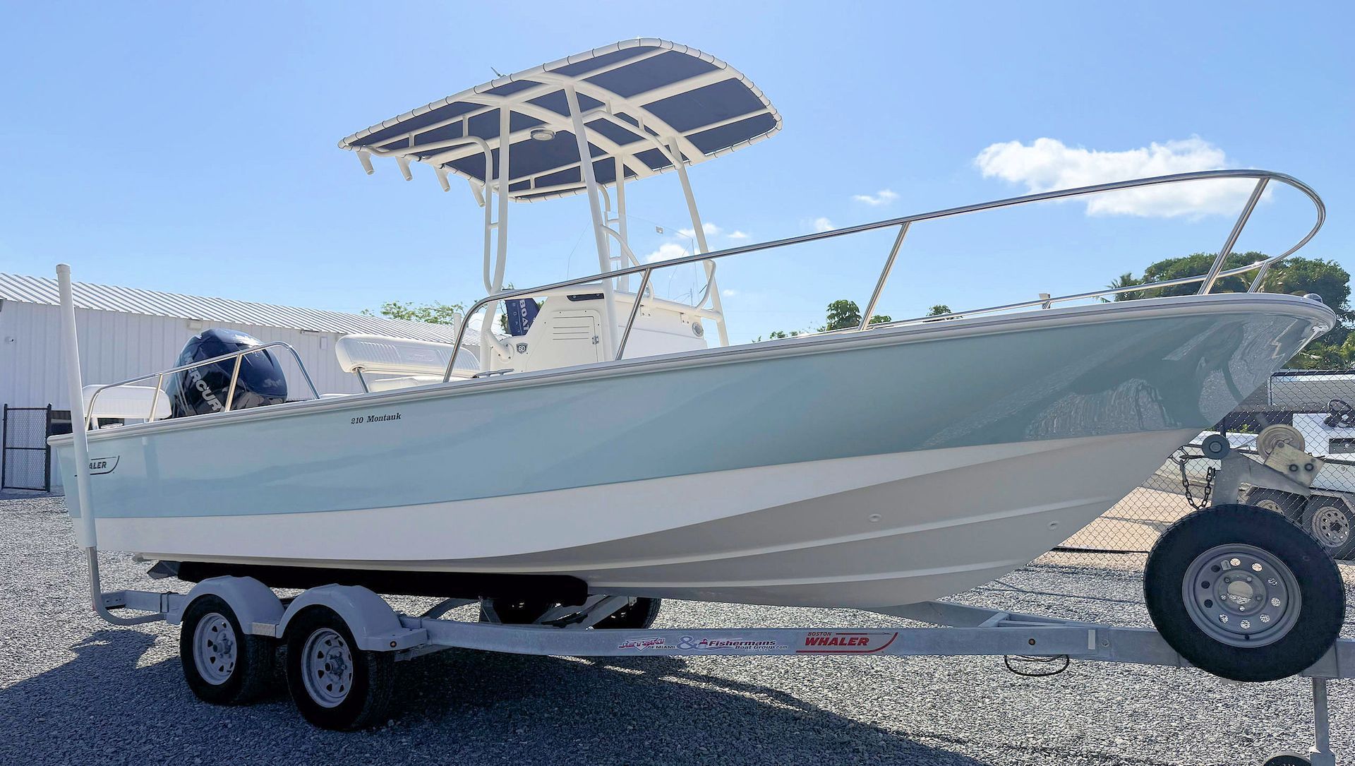 White center-console boat on a trailer in a gravel lot under a blue sky