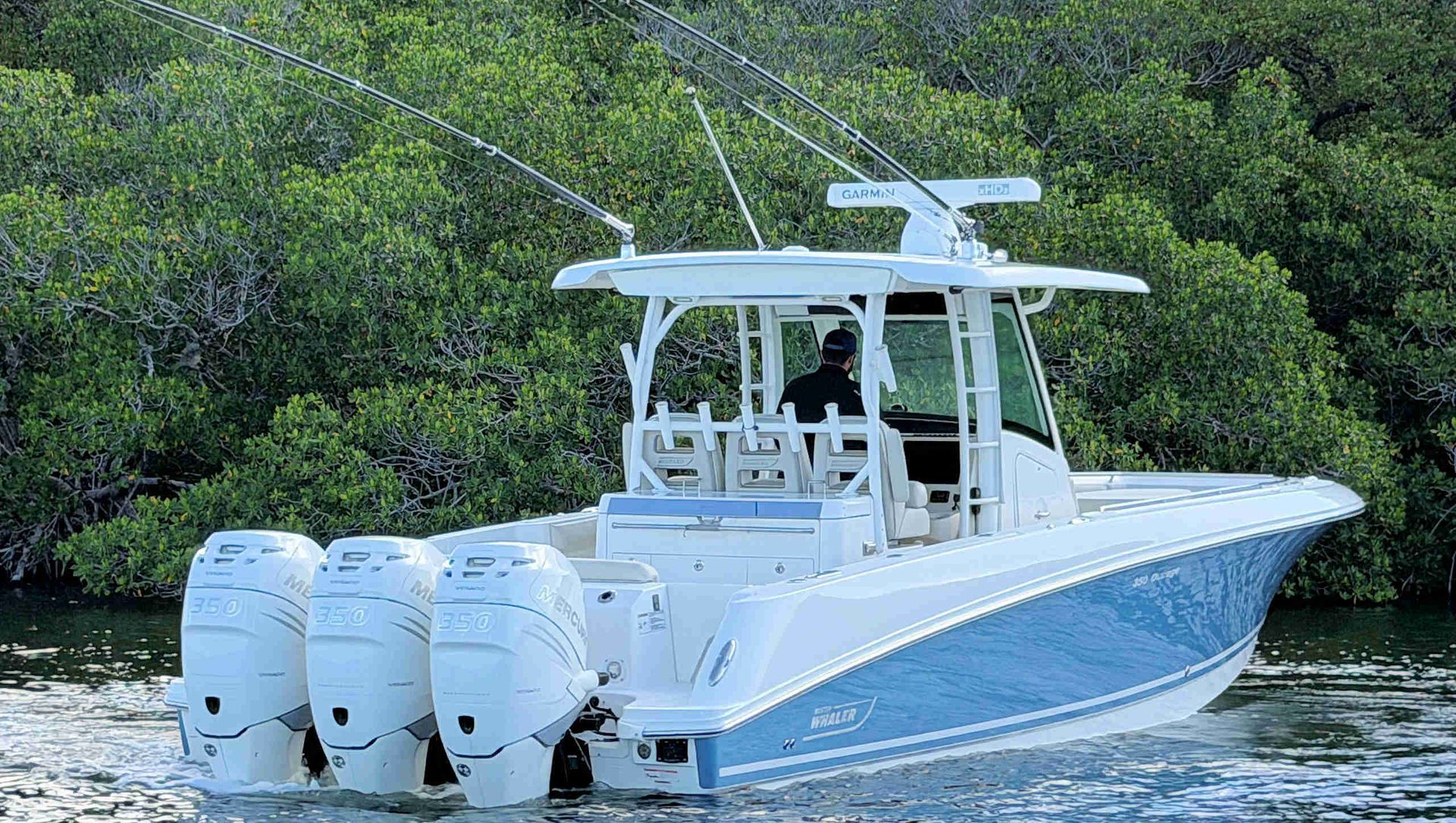 White center-console fishing boat with three outboard motors on calm water near mangroves