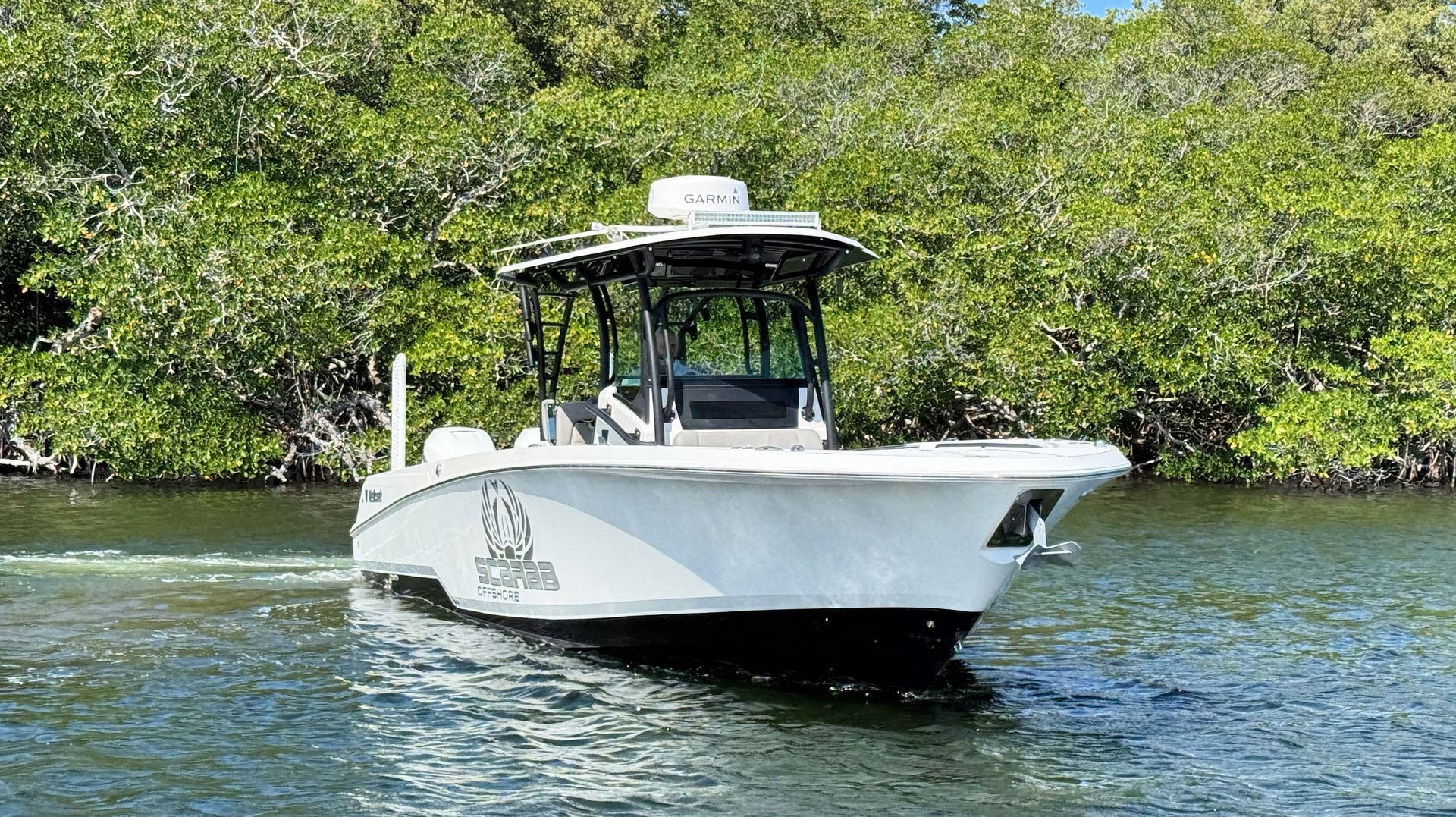 White motorboat cruising on calm water near green mangroves