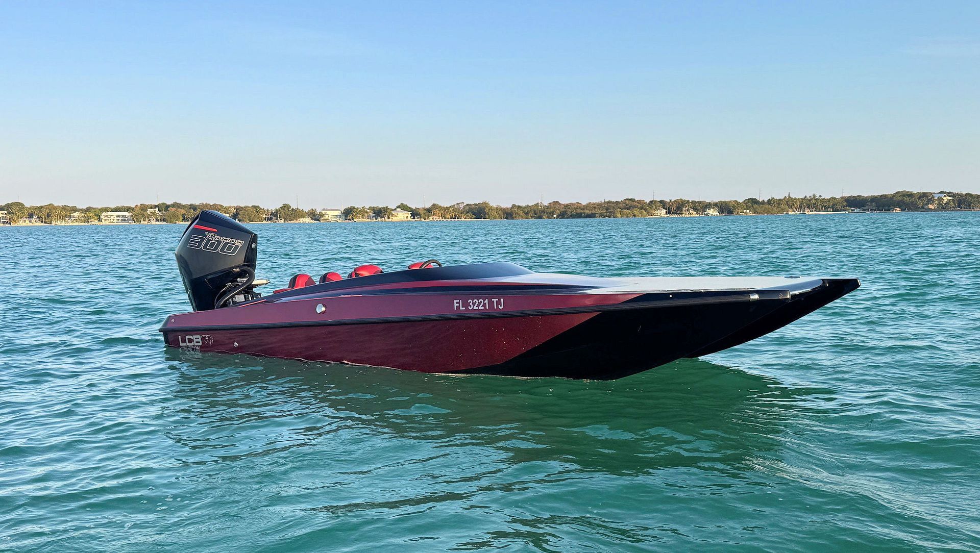 Red high-performance catamaran skimming across blue water near a distant shoreline