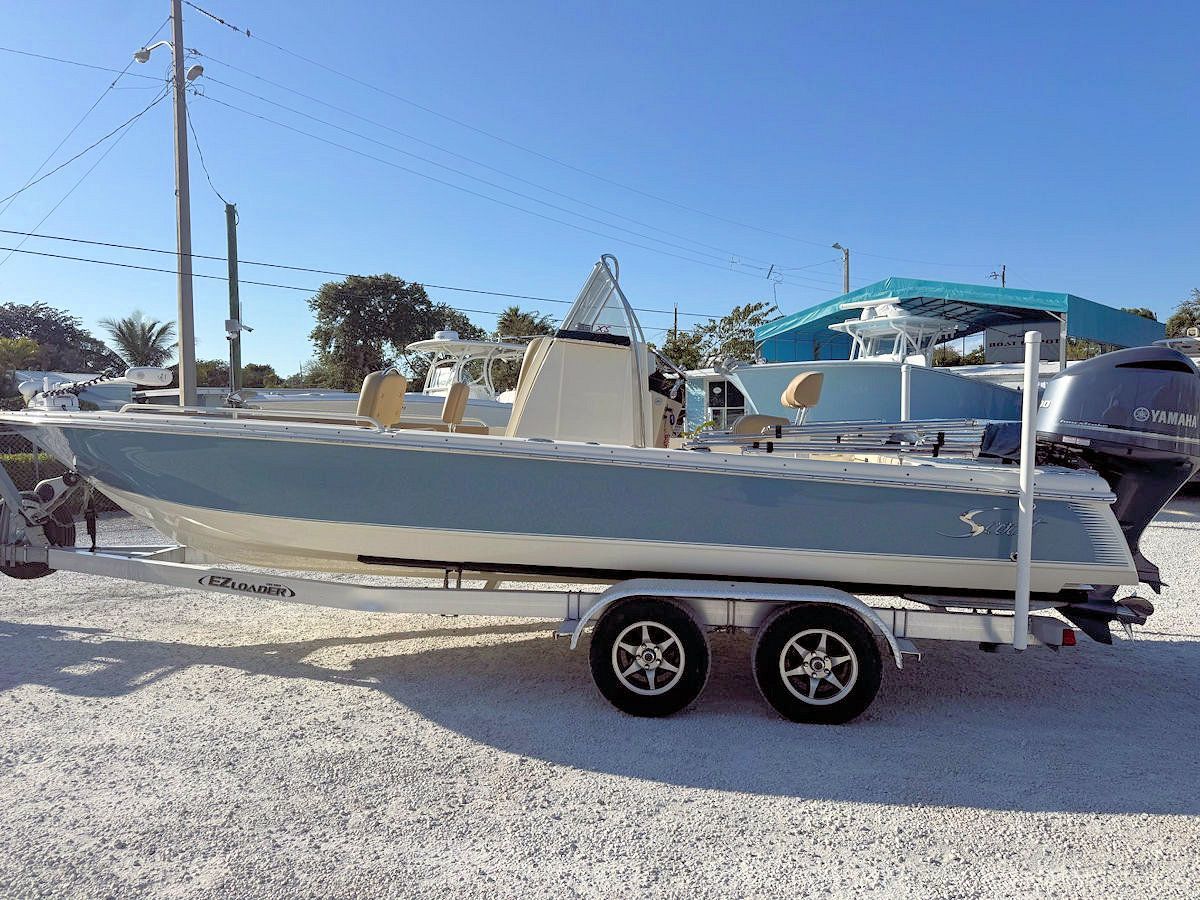 Light blue and beige fishing boat on a trailer, under a clear blue sky.