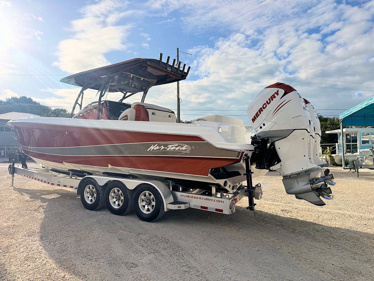 A red and white motorboat on a trailer, with a white outboard motor, parked outside on a sunny day.