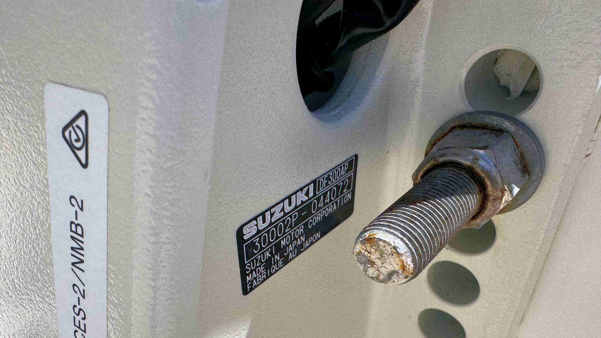 Close-up of a metal threaded stud protruding from a gray machine panel with engine label.