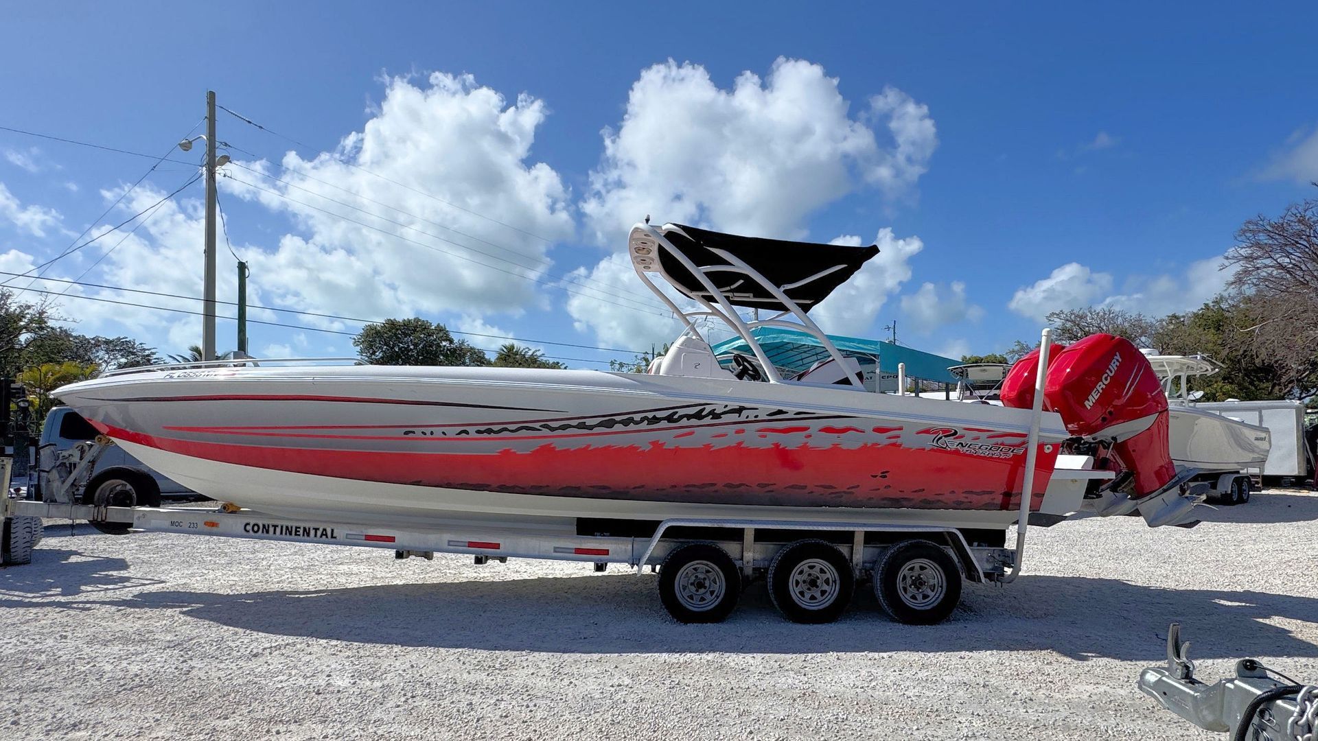 White and red speedboat on a trailer in a gravel lot under a blue sky with clouds.