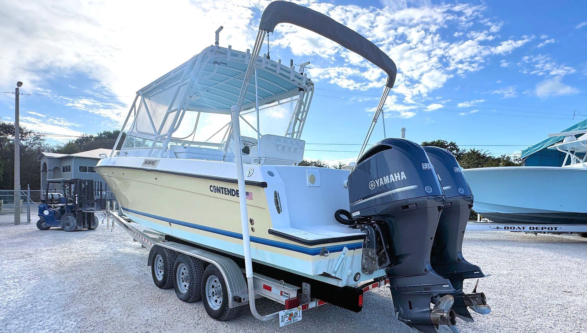White cabin boat on a trailer with twin outboard motors at a marina under a blue sky