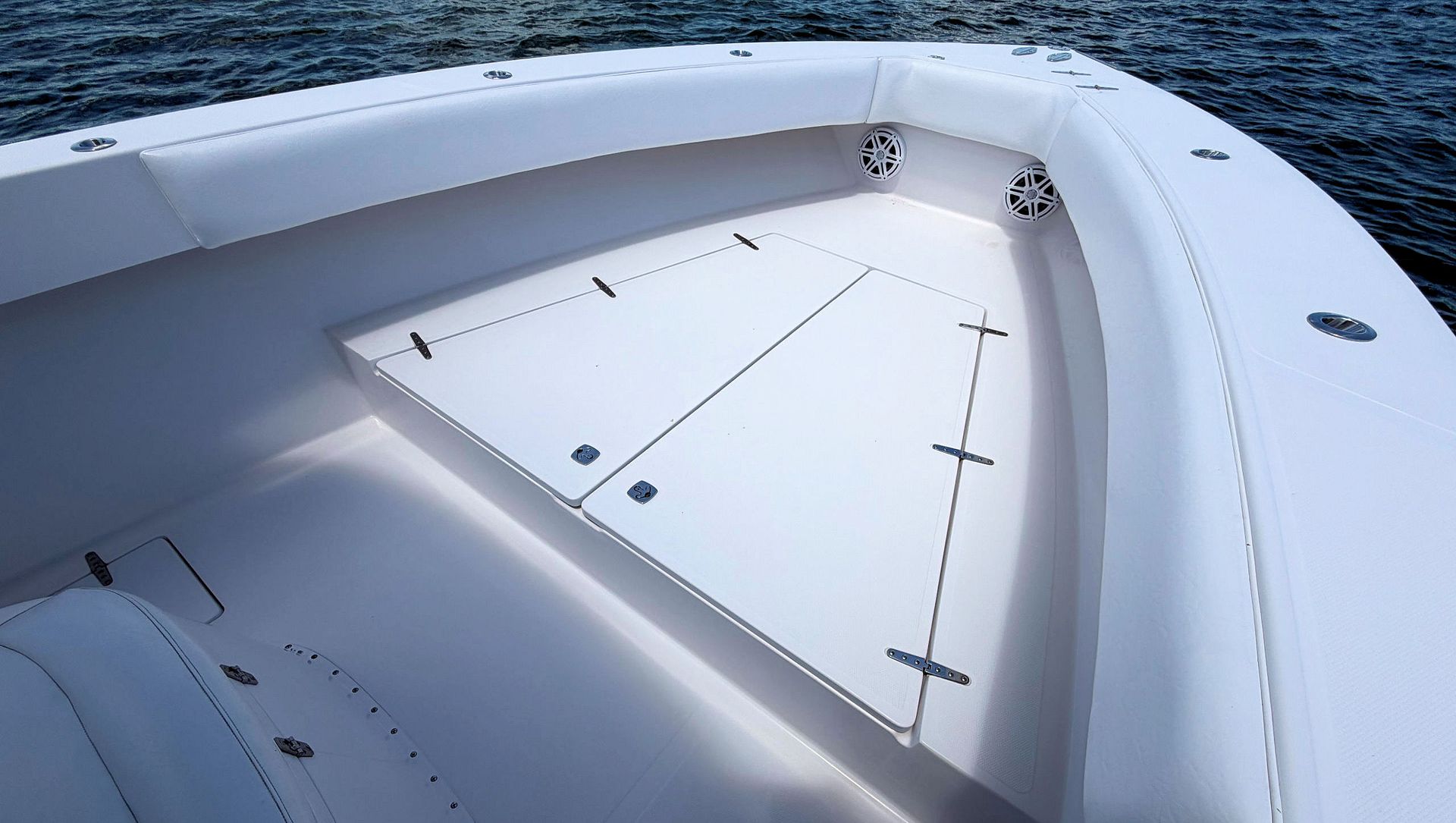 White boat deck with storage hatches and curved seating area near the water