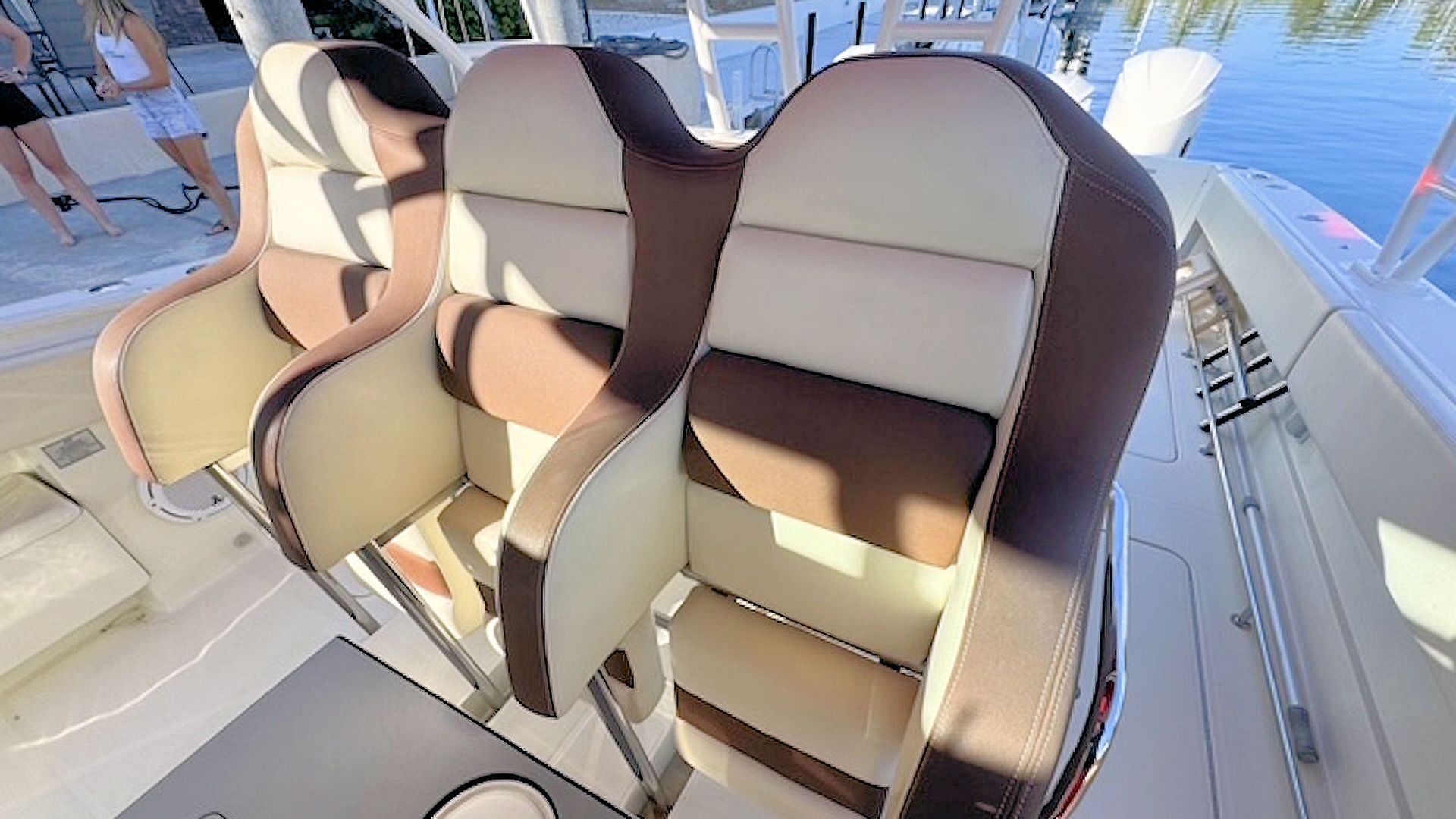 Three cushioned boat seats in tan and brown on a aftdeck, with water visible in the background.
